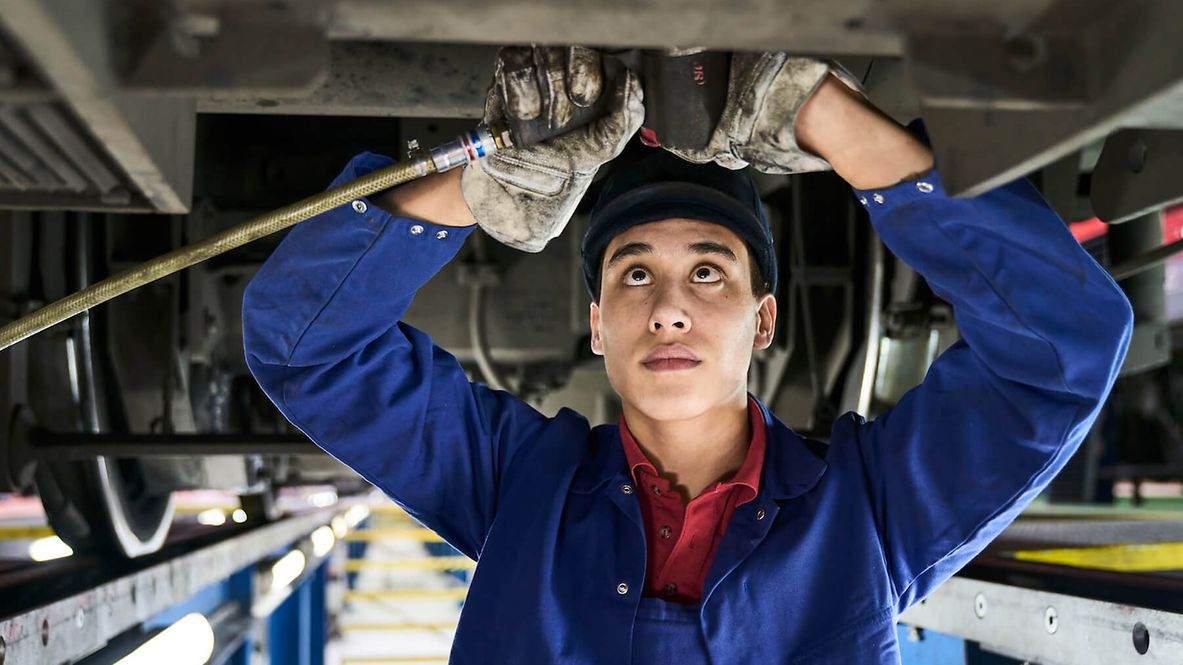 Ein Mann steht unter einem Zug und repariert ihn. Der Blick des Mannes ist nach oben gerichtet.