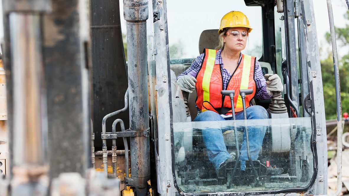Eine Mitarbeiterin sitzt im Führerhaus eines Baugeräts und bedient mehrere Hebel.