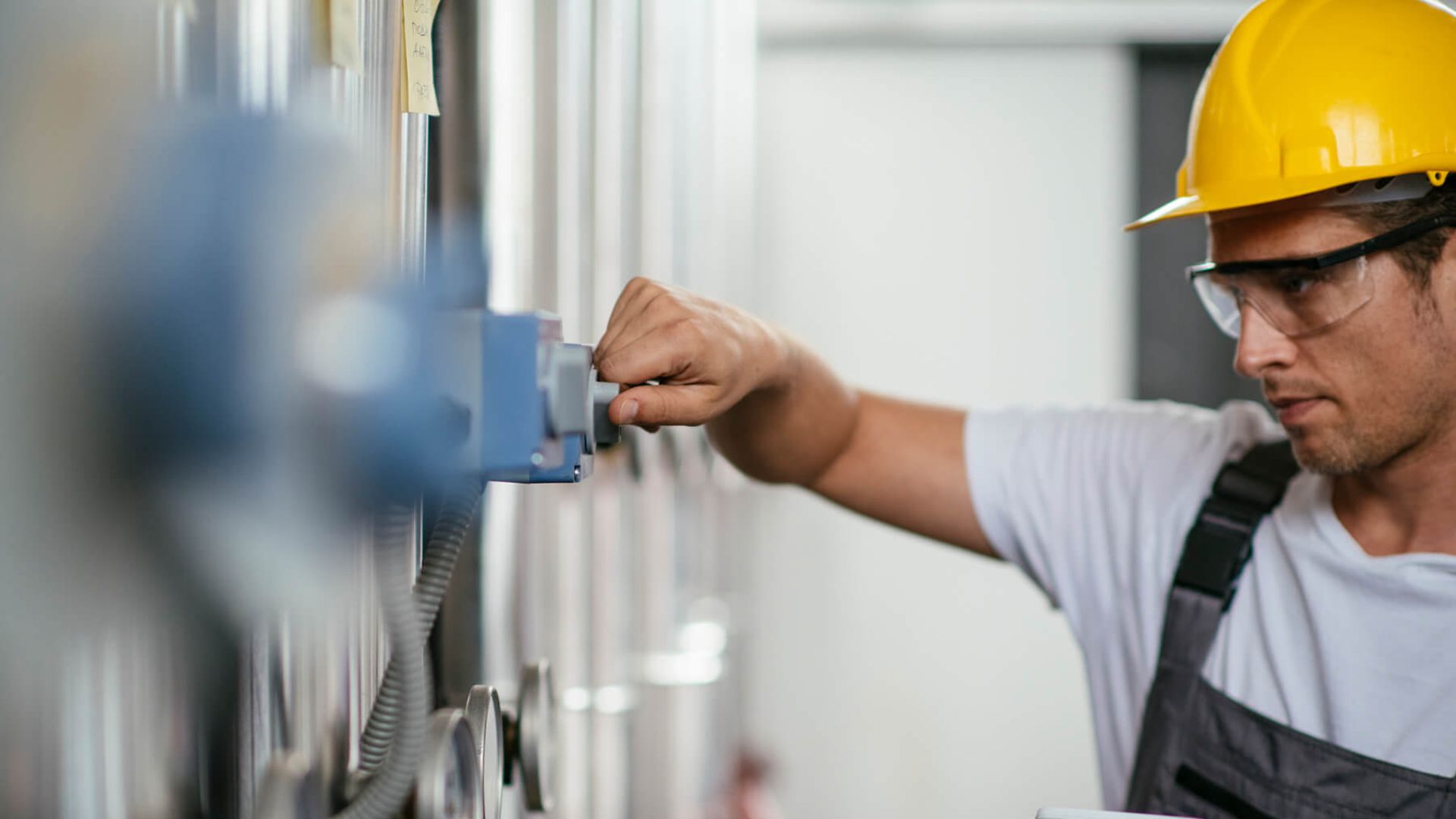 Eine Person mit gelbem Helm und Arbeitskleidung schaut intensiv auf eine Maschine.