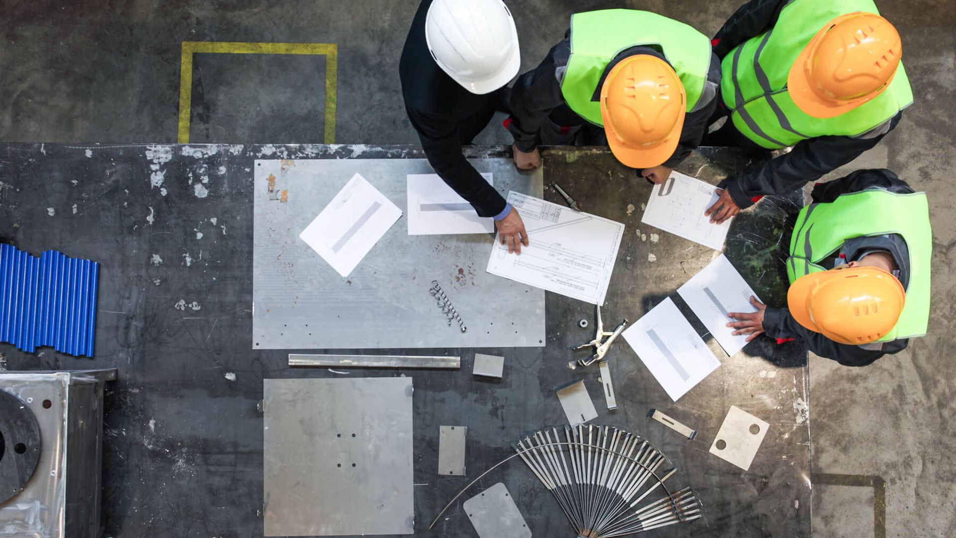 Vier Personen mit Warnweste und Schutzhelm stehen an einem Tisch und besprechen etwas.
