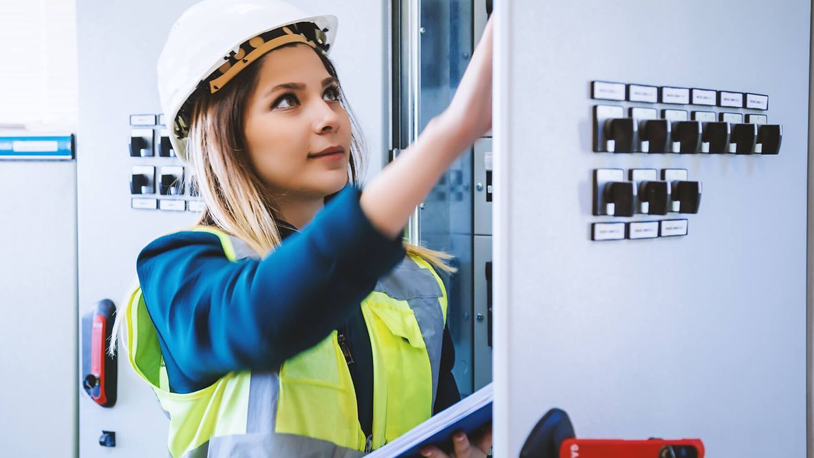 Eine Frau mit Warnweste und Schutzhelm betrachtet etwas auf der Innenseite einer Tür. Und hat ein Tablet in der Hand.