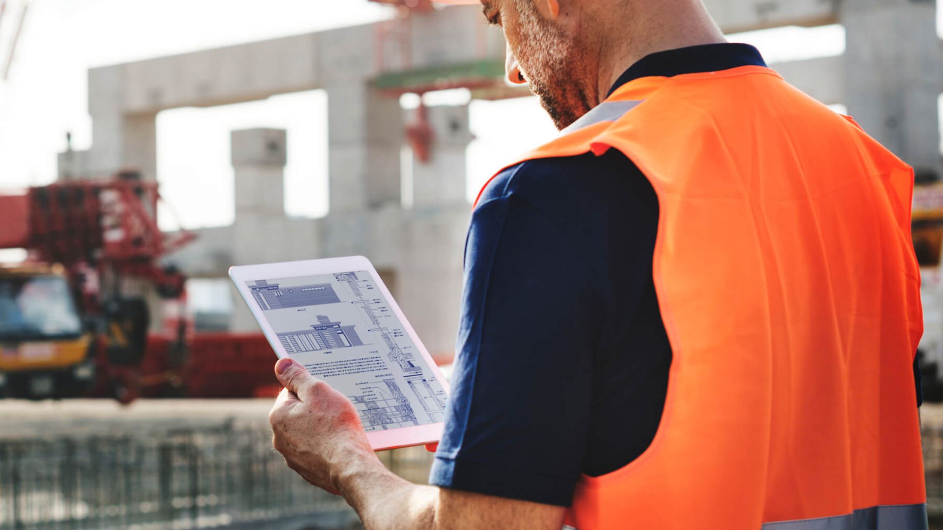 Ein Mann sichtet technische Zeichnungen auf einem Tablet. Es sind Grund- und Aufrisse zu sehen. 