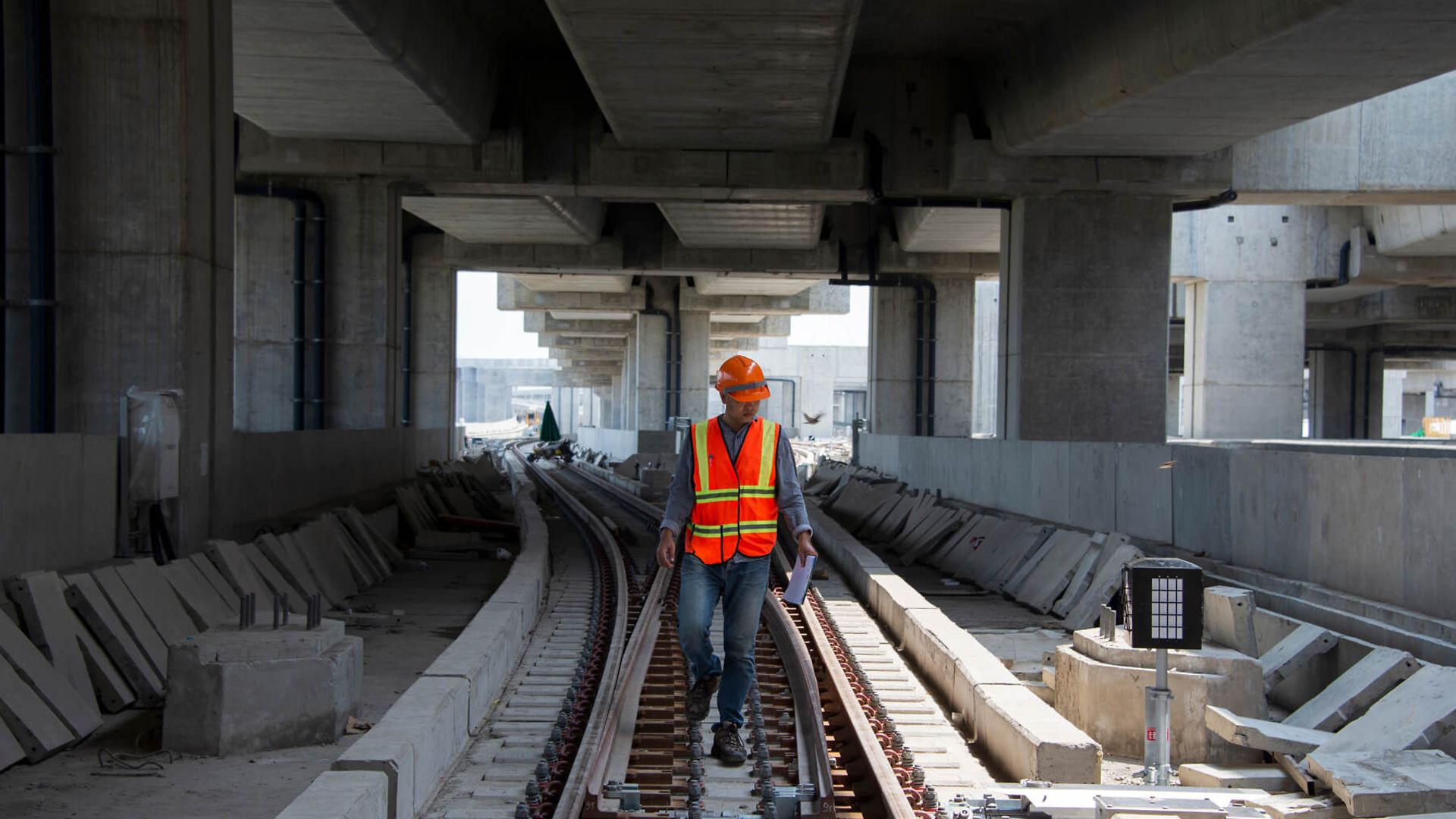 Ein Mann in Schutzkleidung läuft unter einer Brücke zwischen den Gleisen auf den Betrachter zu.