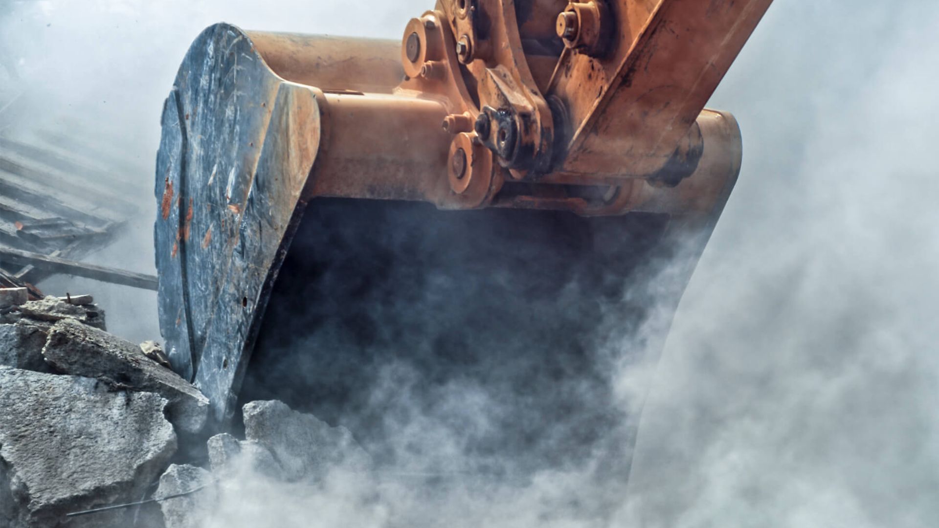 Ein Baggerarm gräbt sich in den Boden rein. Dadurch entsteht eine Staubwolke