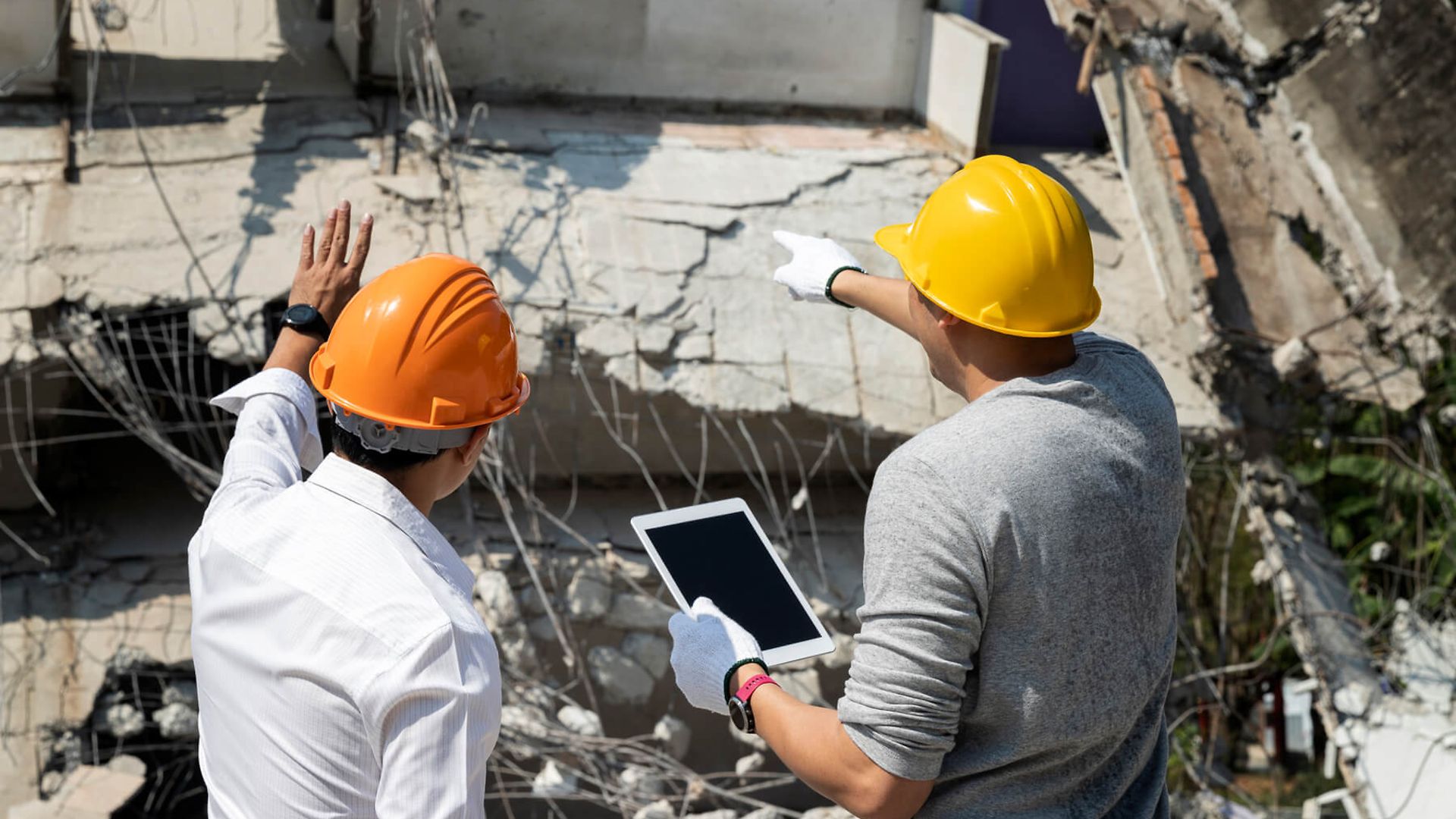Zwei Arbeiter unterhalten sich über die Trümmer hinter ihnen.