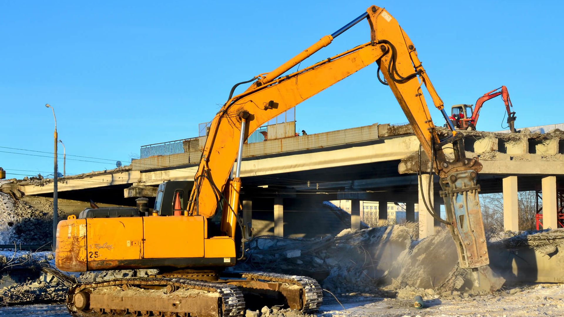 Ein Bagger steht auf einer Baustelle. Im Hintergrund ist ein teilweise abgerissenes Gebäude.