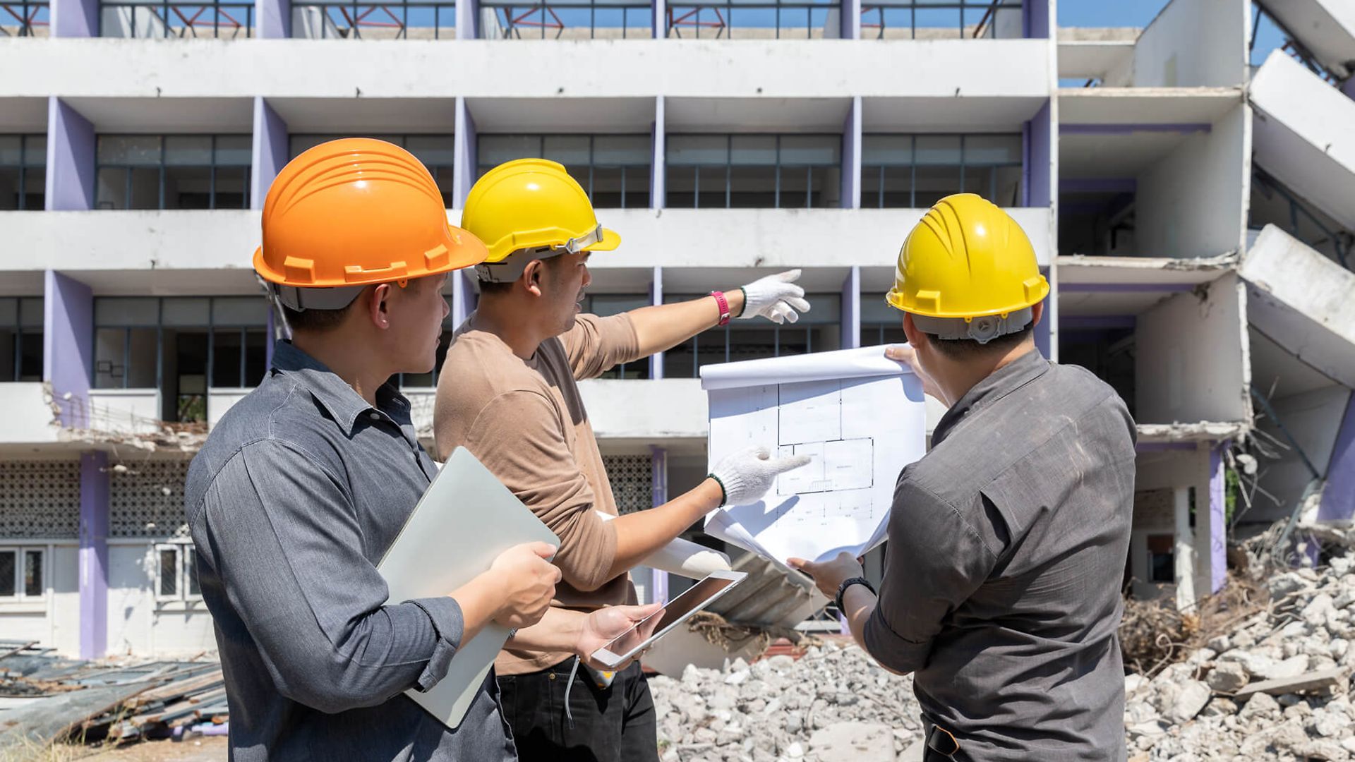 Drei Personen unterhalten sich über das dahinter stehende Gebäude. Sie halten einen Plan in ihrer Hand.