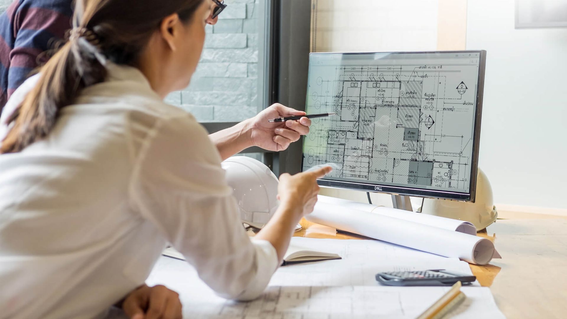 Zwei Personen unterhalten sich und deuten auf einen Grundriss, der auf einem Bildschirm zu sehen ist. 