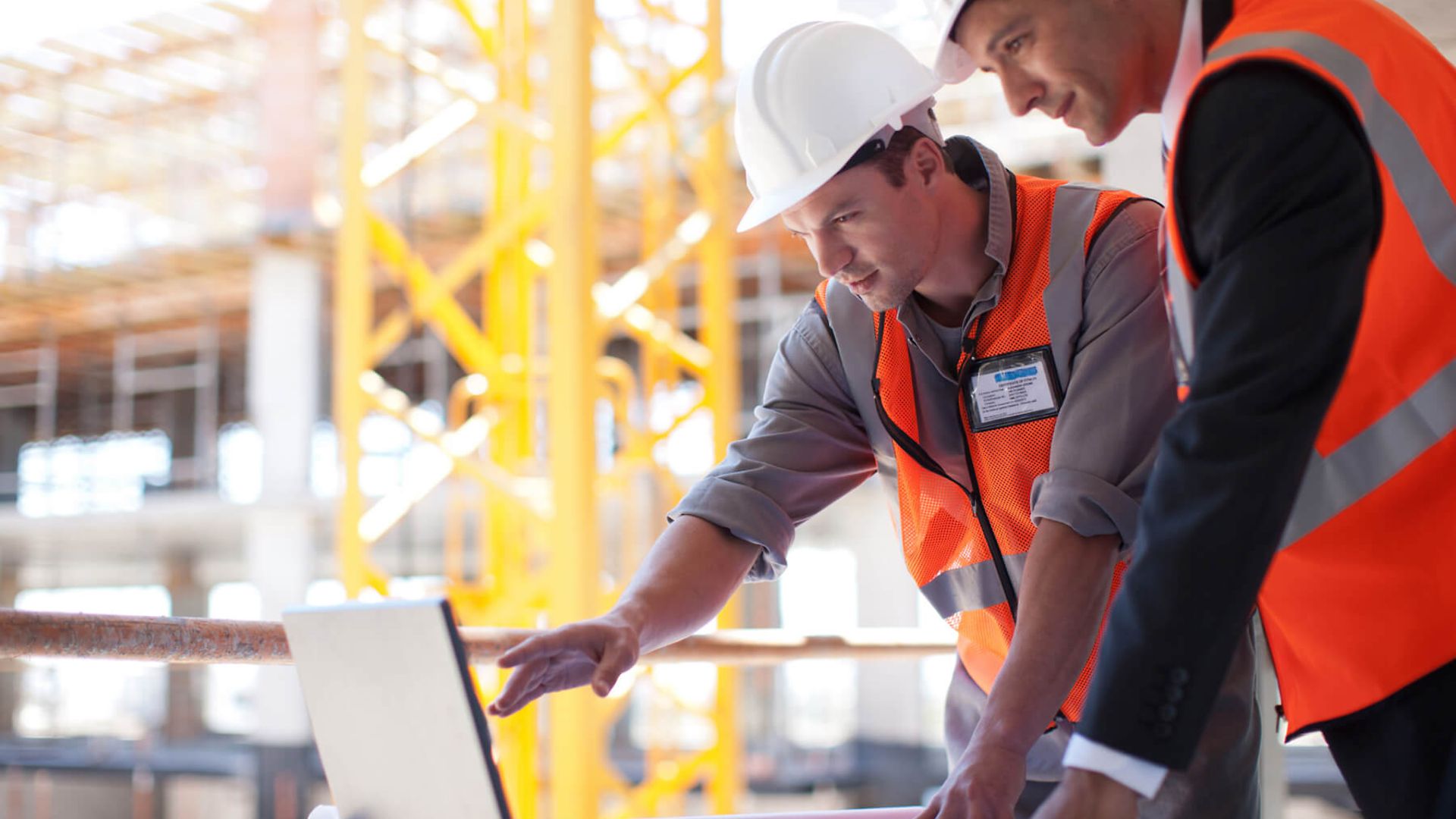Zwei Personen unterhalten sich und schauen währenddessen auf den Laptop. Im Hintergrund ist eine Baustelle.
