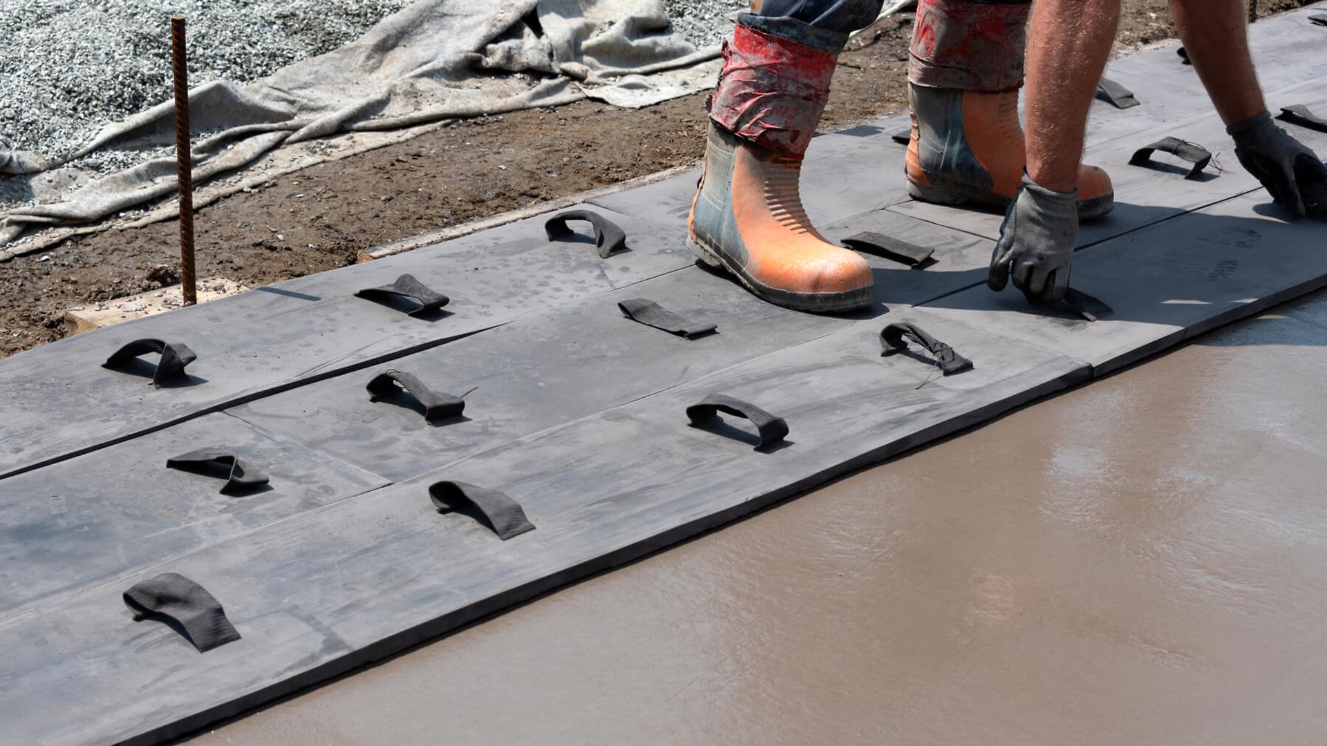 Eine Person mit Gummistiefeln und Handschuhen drückt mit Hilfe von speziellen Latten den Beton platt.