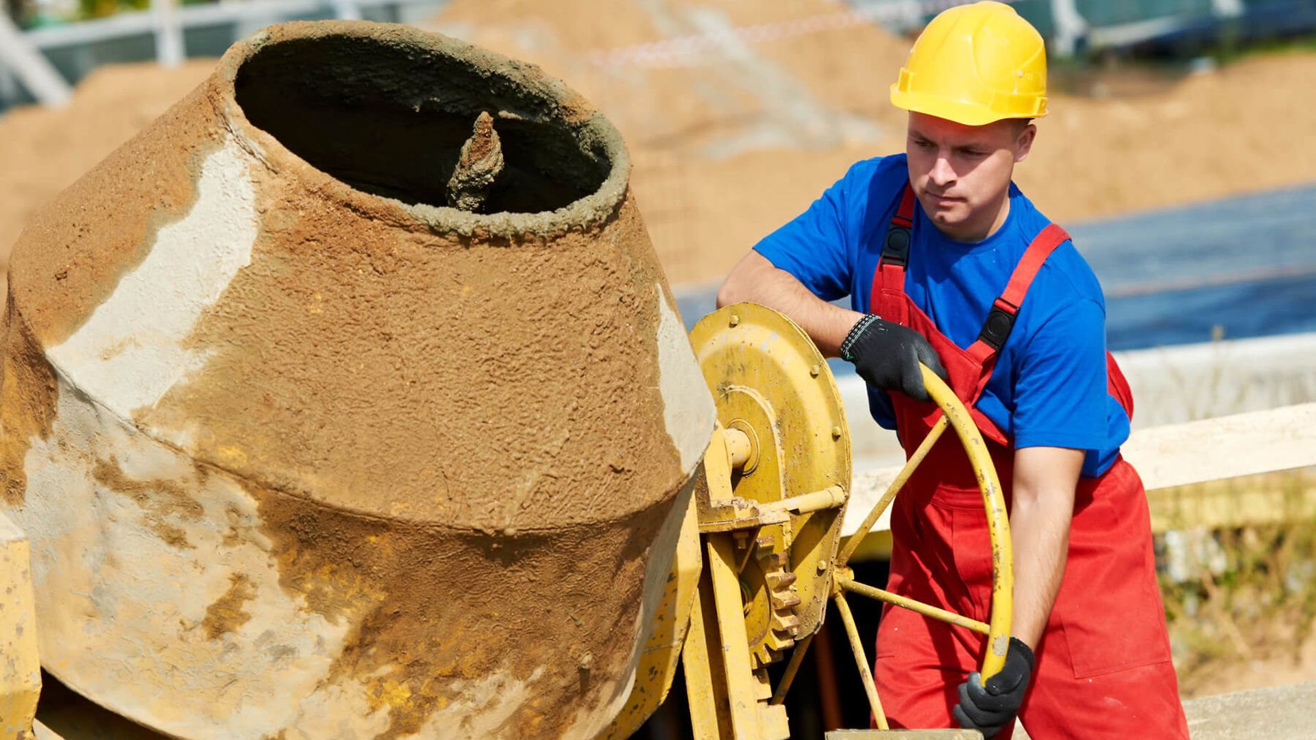 Ein Arbeiter in Latzhose mit Helm steht an einem Betonmischer.
