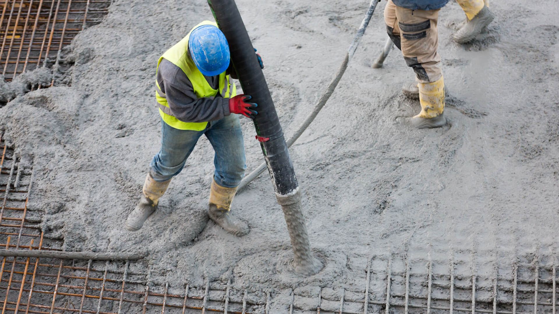 Eine Person ind Arbeits- und Schutzkleidung, die auf der Stahlarmierung einer unfertigen Betondecke steht