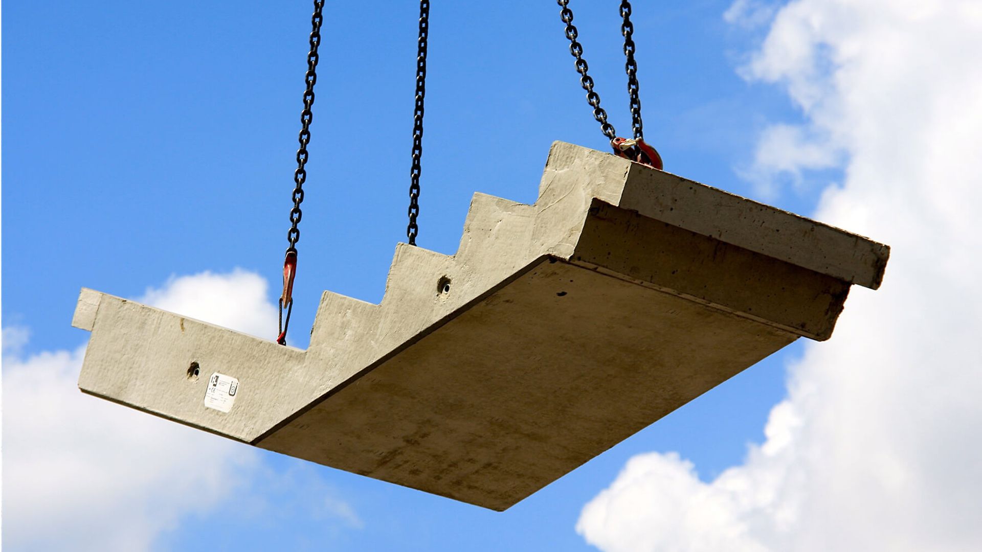Ein Teil einer Betontreppe wird mit Seilen verladen. Sie schwebt gerade in der Luft.