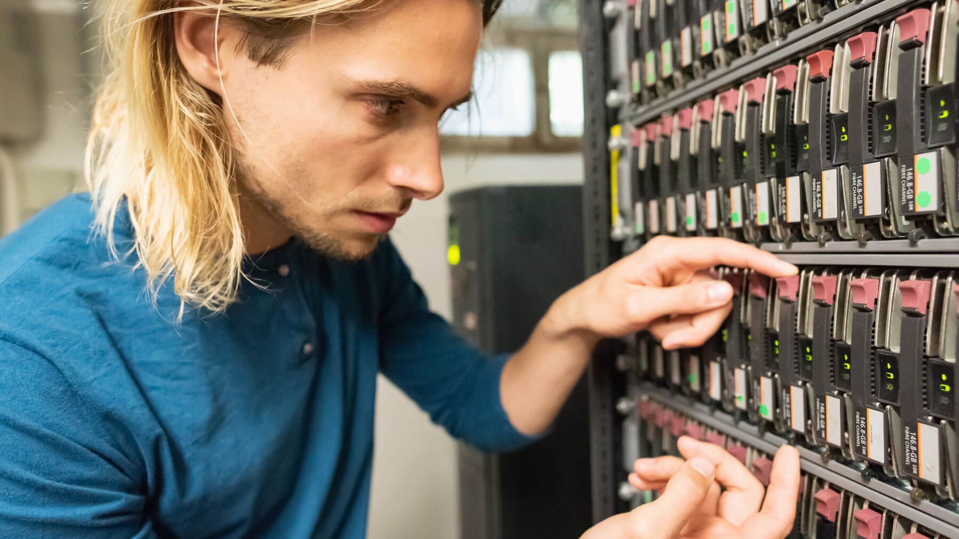 Ein Mann der an einem greift nach einer Festplatte in einem großen Server.