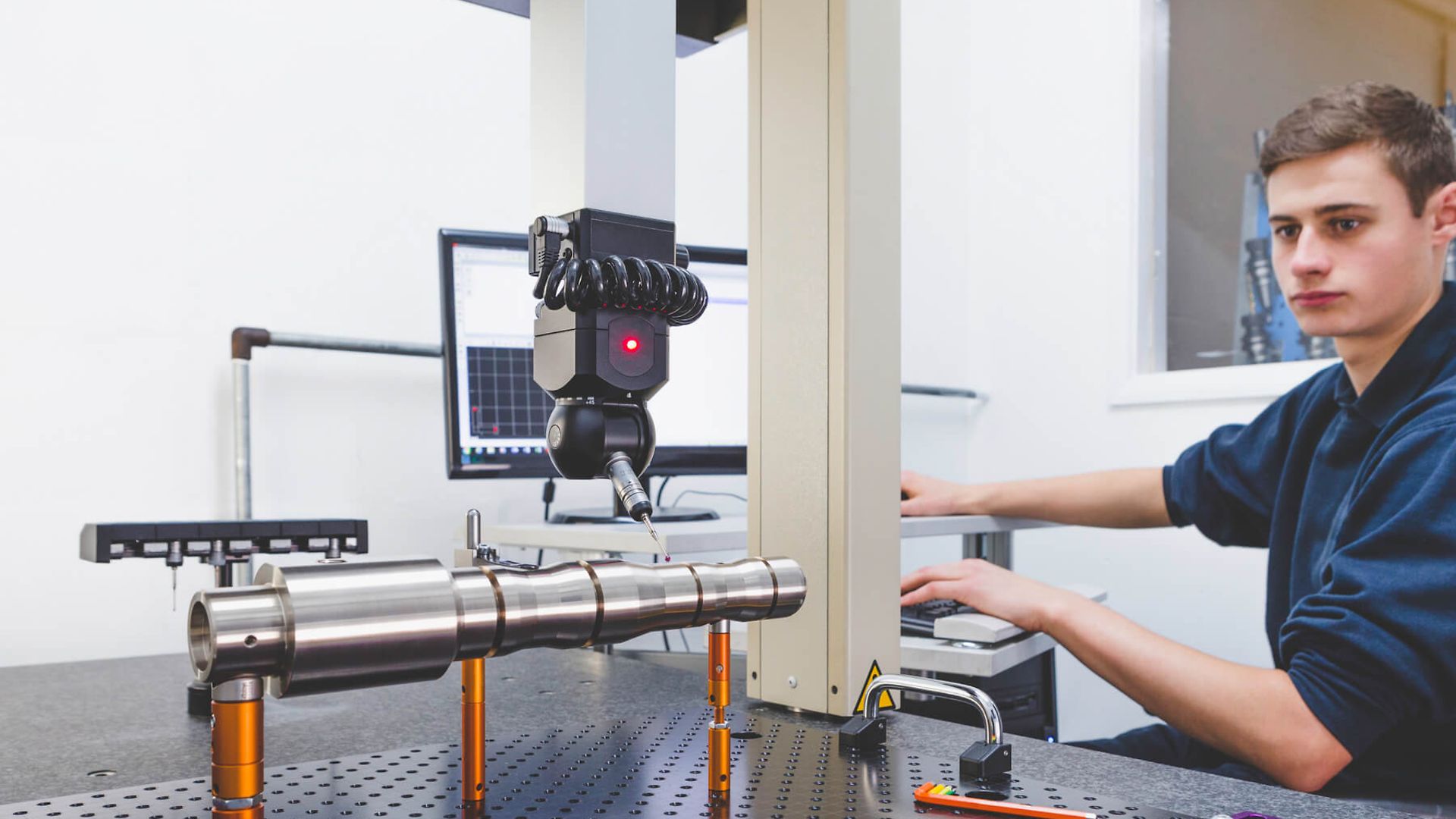 Ein Junge der in einem Werkraum mit einem Computer den Arm einer Maschine bedient. 