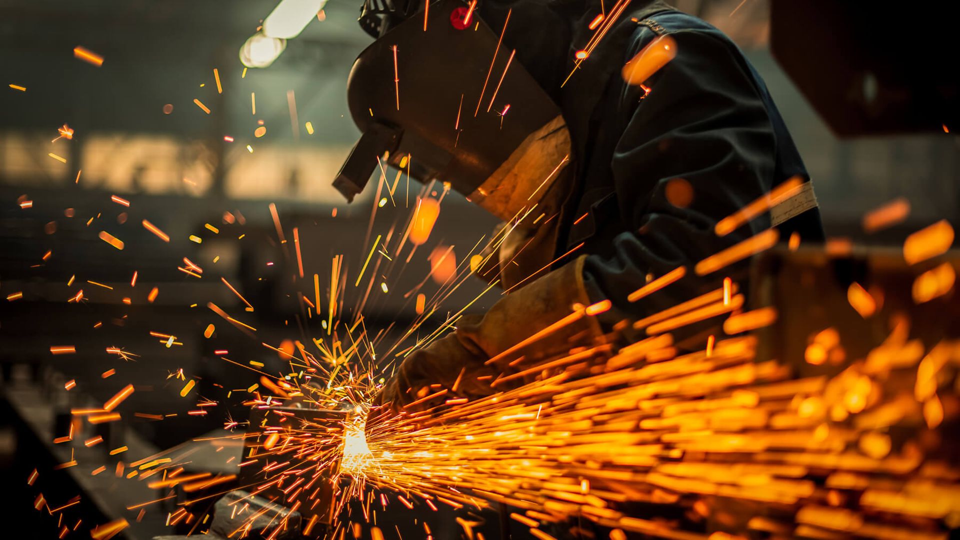 Eine Person mit Schutzkleidung fräßt Metall. Dadurch entstehen Funken.