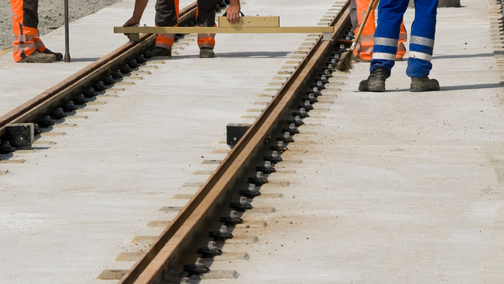 Mehrer Arbeiter halten eine Messlatte zwischen die Gleise.