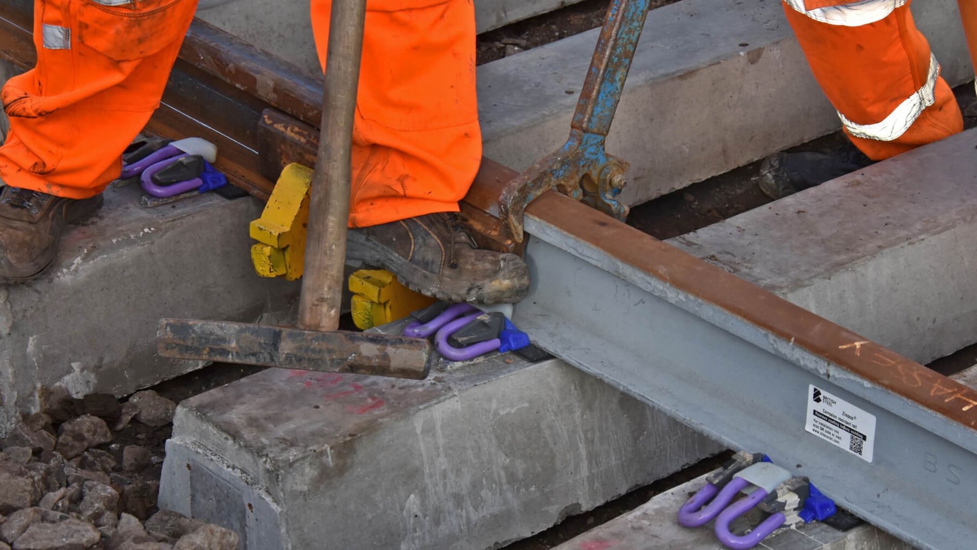 Detailaufnahme eines Gleises, das gerade mit einer Zange und einem Hammer bearbeitet wird.