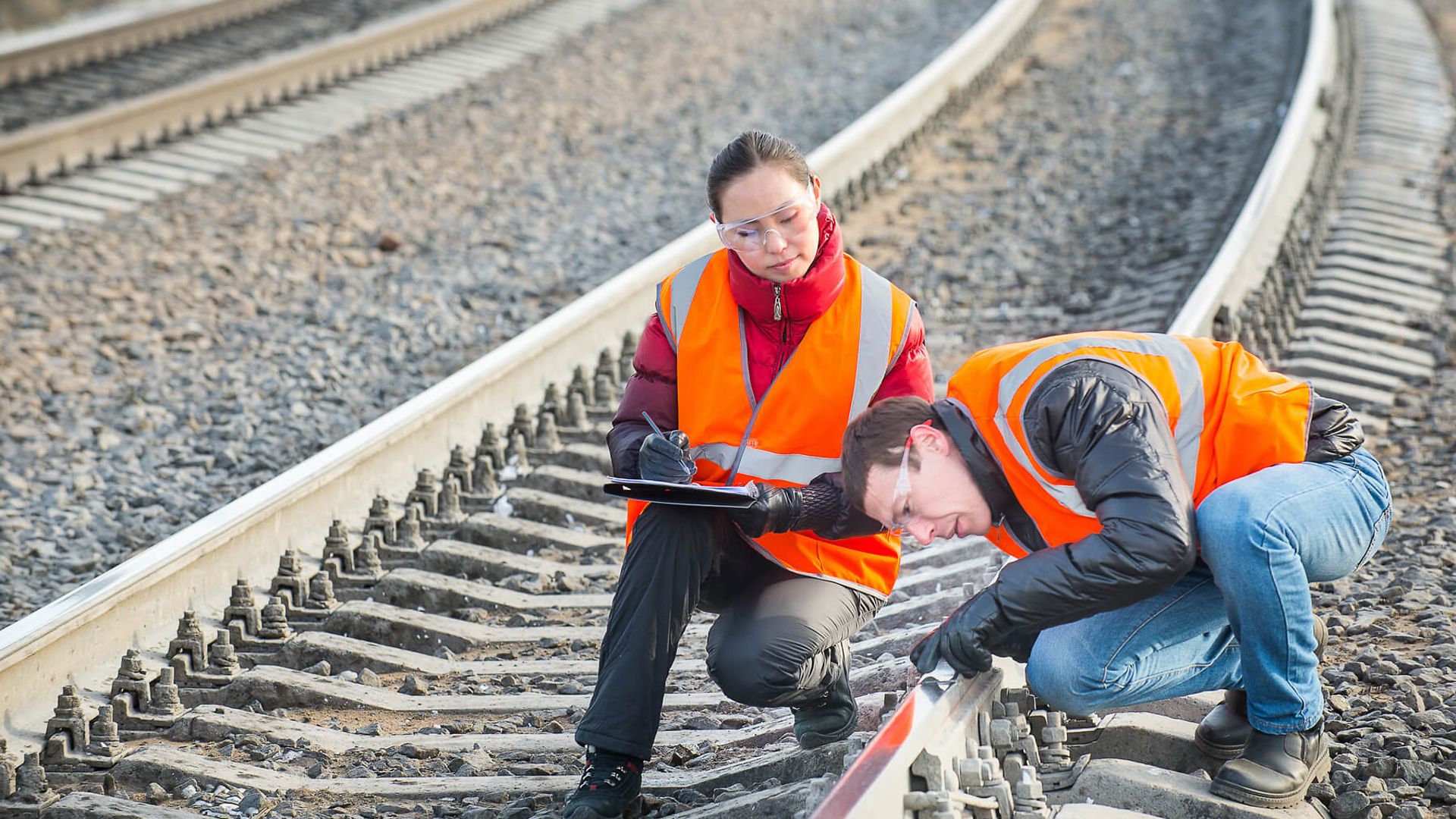 Zwei Personen überprüfen die Gleise. Eine Person ist über das Gleis gebeugt und fährt mit der Hand daran entlang