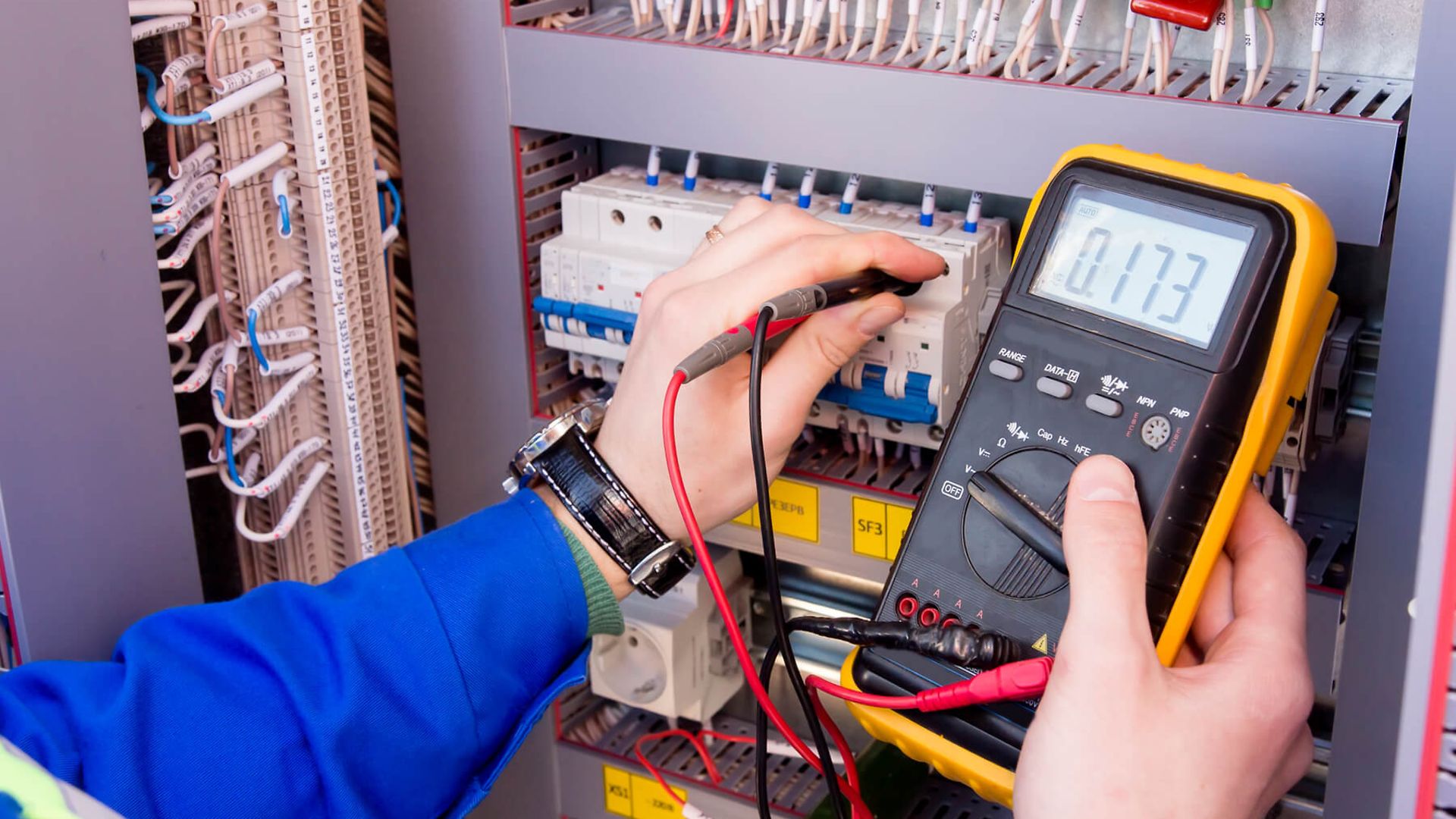 Aufnahme eins Spannungsmessgerätes, das gerade von einer Person mit einem Sicherungskasten verbunden wird.