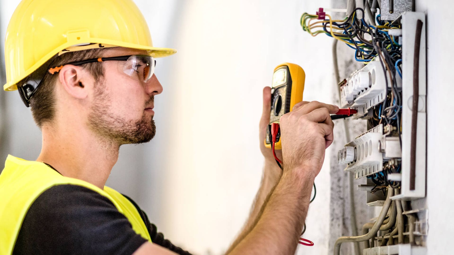 Ein Mann ließt die Werte eines Spannungsmessgerätes ab, das er gerade an die Leitungen eines Sicherungskastens hält.