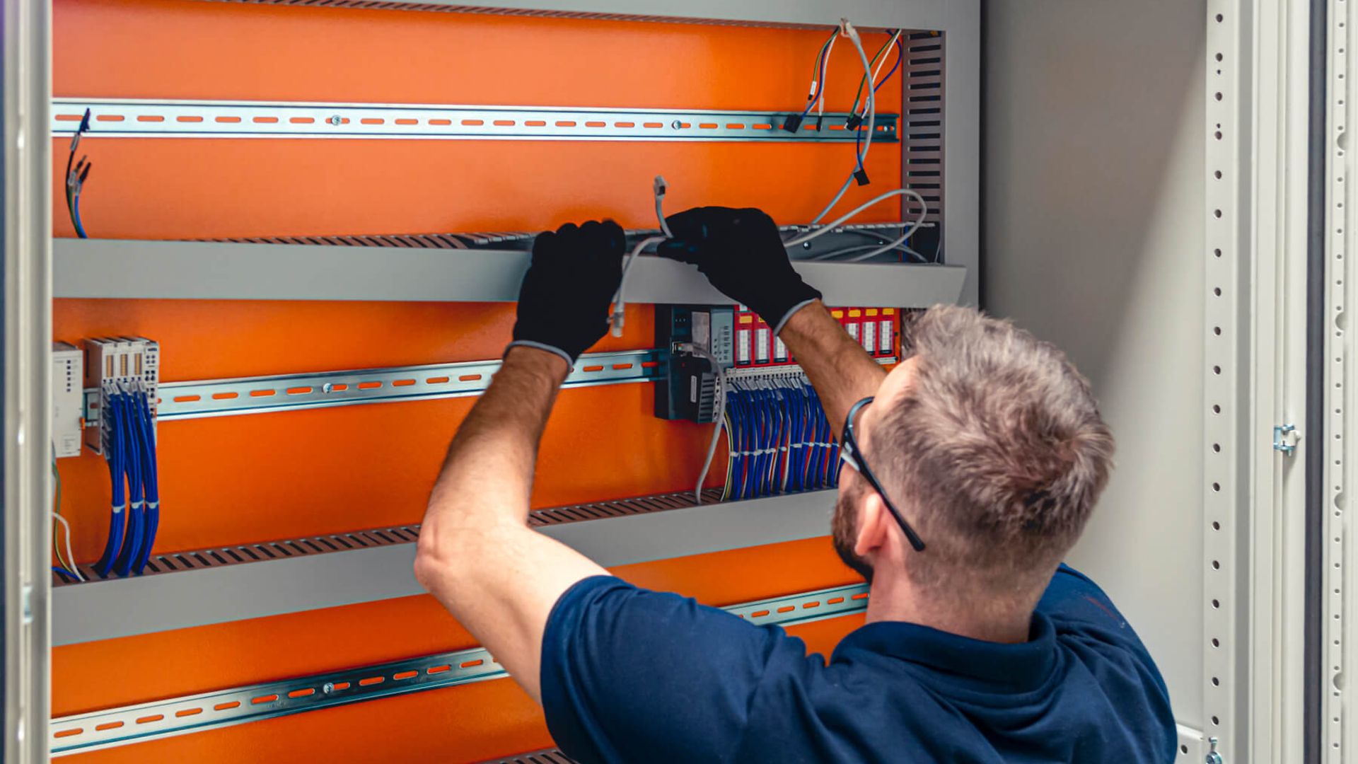 Ein Mann verlegt Kabel und montiert Sicherungen in einem Metallschrank oder Sicherungskasten.