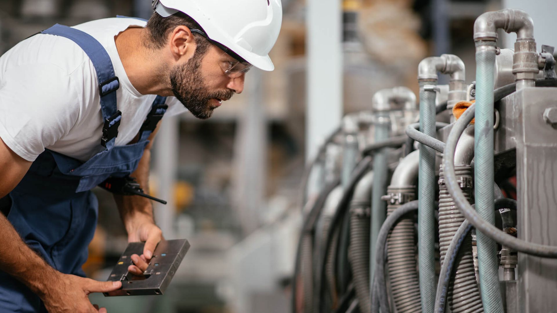 Ein Mann in Latzhose und Schutzhelm betrachtet intensiv eine Maschine.