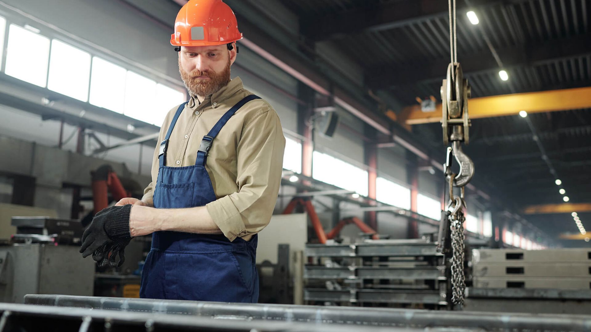 Ein Mann mit blauer Latzhose und orangenem Helm steht vor einer Werkbank
