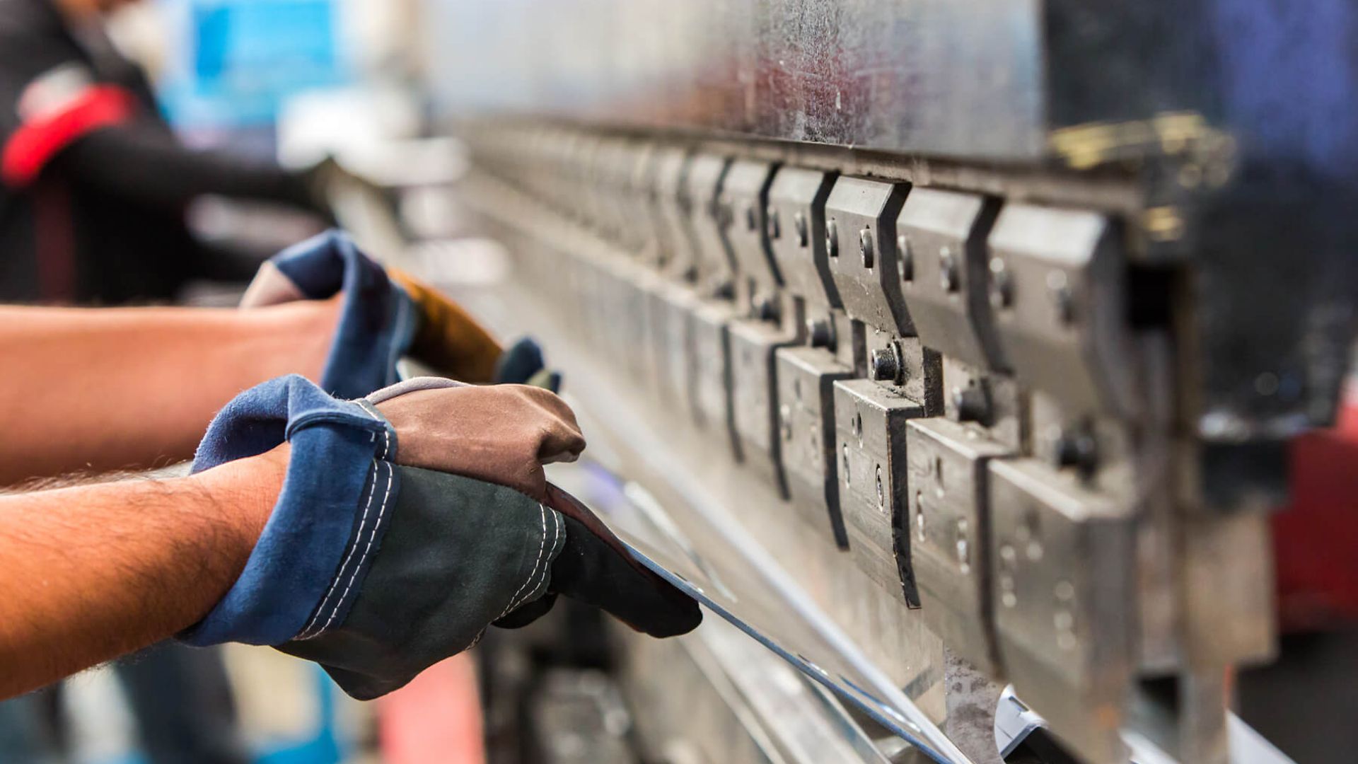 Arbeiter mit Handschuhen halten eine Metallplatte in eine Maschine zum Stanzen oder Schneiden.
