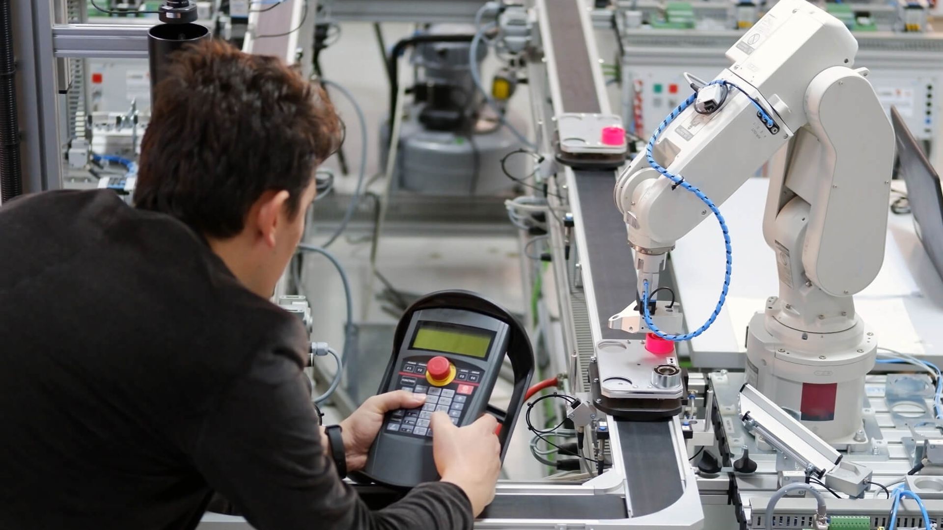 Ein Mann steht an einer Maschine mit einem elektrischen Arm. Er bedient den Arm mit einer Fernbedienung.