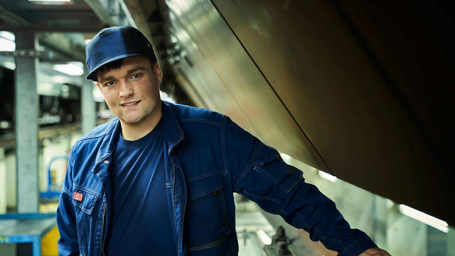 Ein Mann lächelt in die Kamera. Im Hintergrund sieht man einen langen Gang.