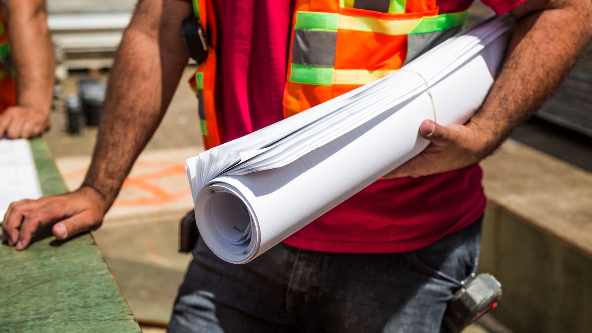 Ein Mann hält gerollte Pläne unter dem Arm. Auf dem Bild ist nur der Oberkörper des Mannes zu sehen.