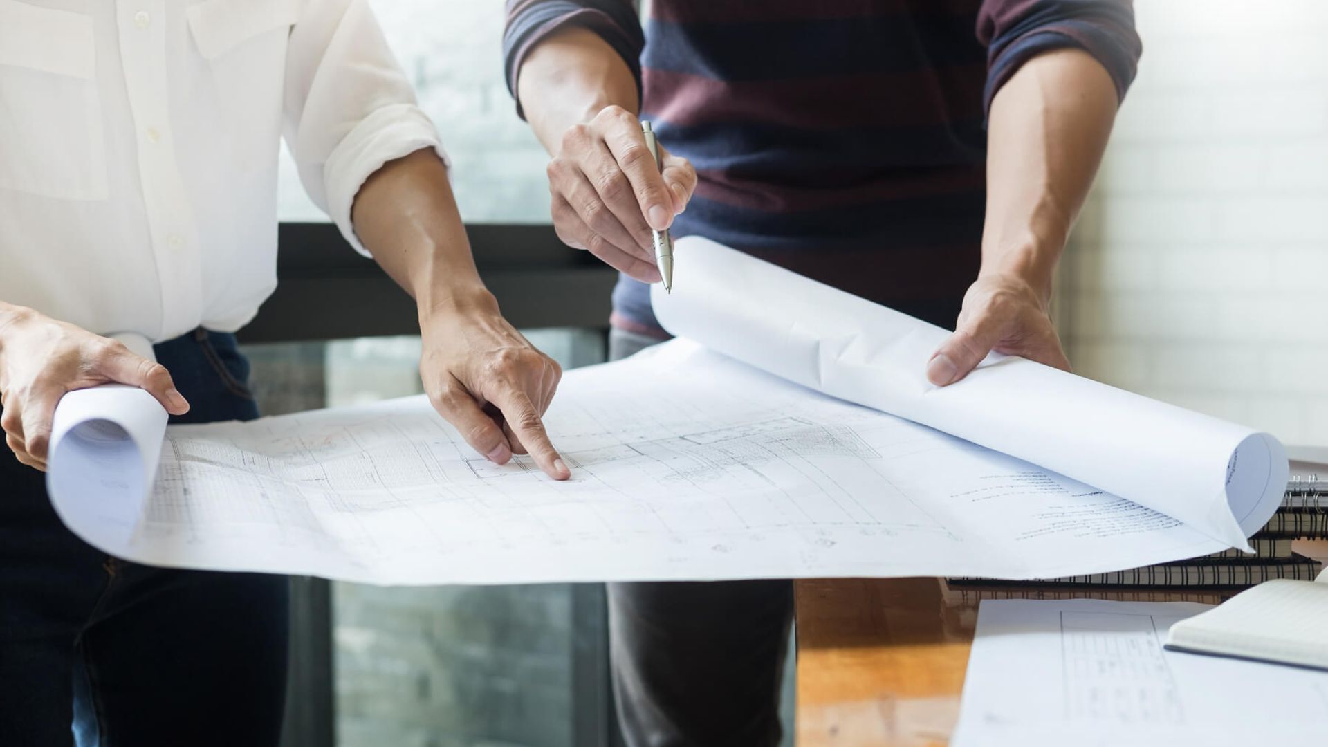Zwei Personen deuten auf einen ausgerollten Plan. Auf dem Bild sind nur der Plan und die vier Hände zu sehen.