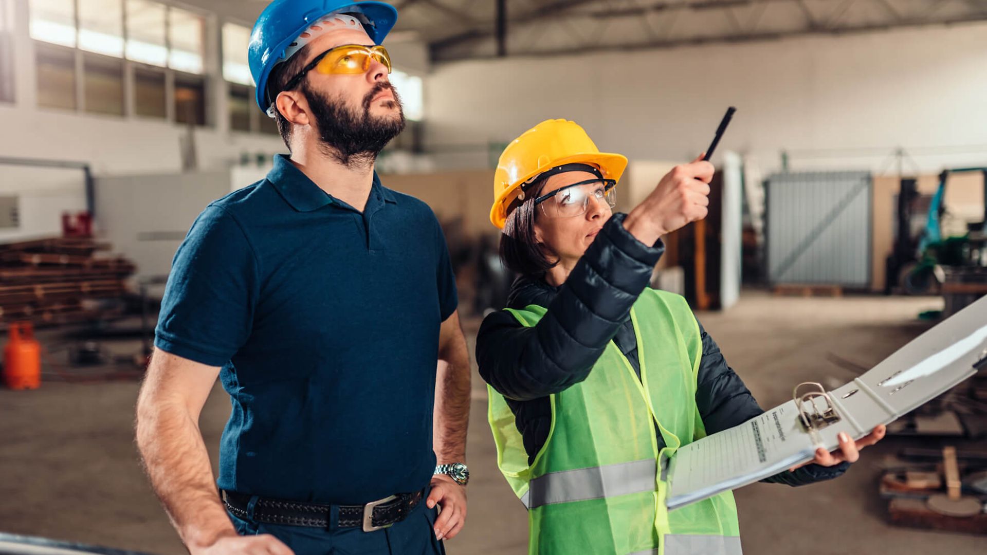 Eine Frau hält ein Ordner und zeigt mit dem Stift auf etwas, dabei erklärt Sie dem Mann, der neben ihr steht, etwas.