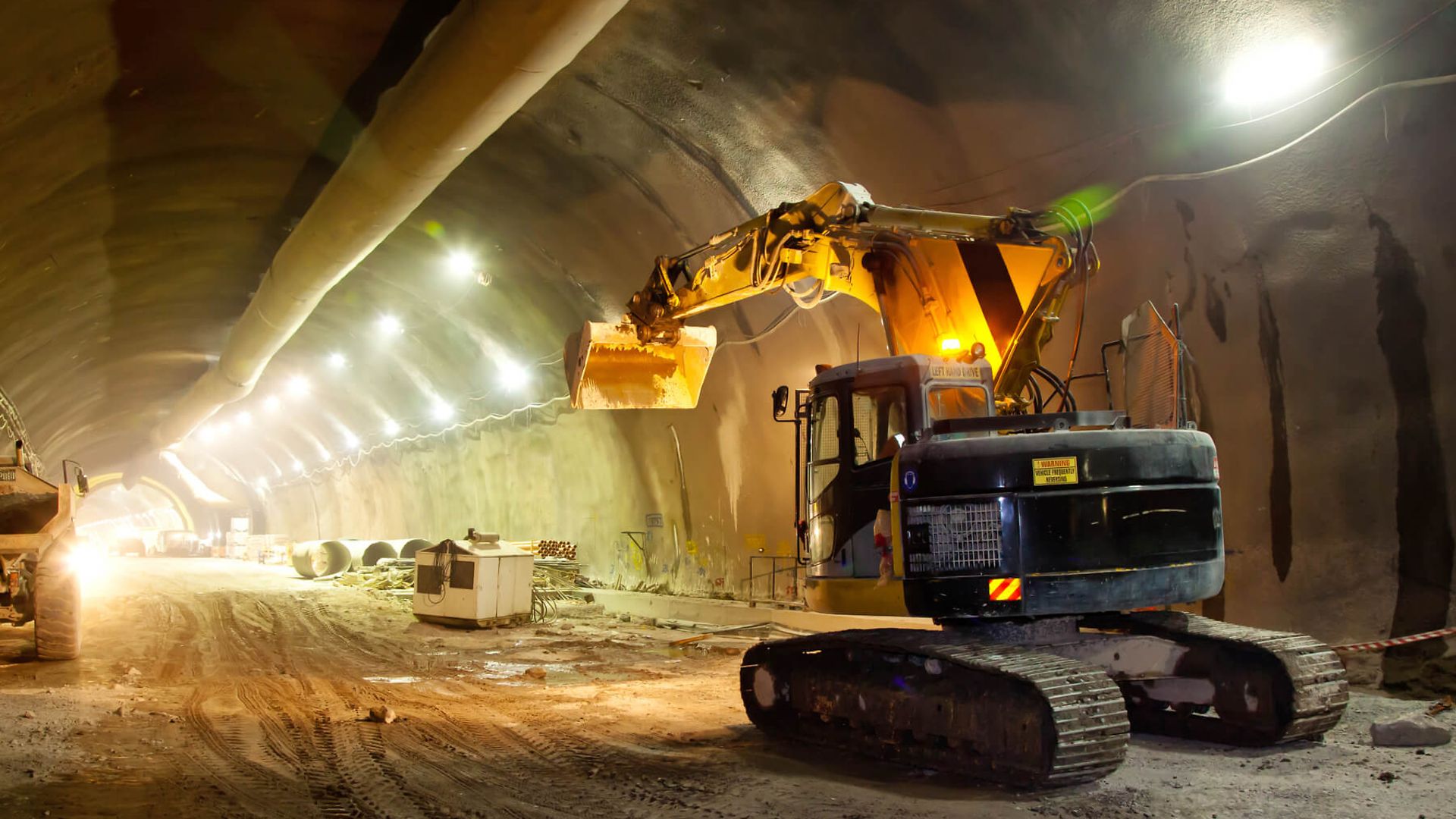 Ein Bagger steht im Rohbau eines Tunnels. Der Boden ist sandig und die Wände noch erdig.