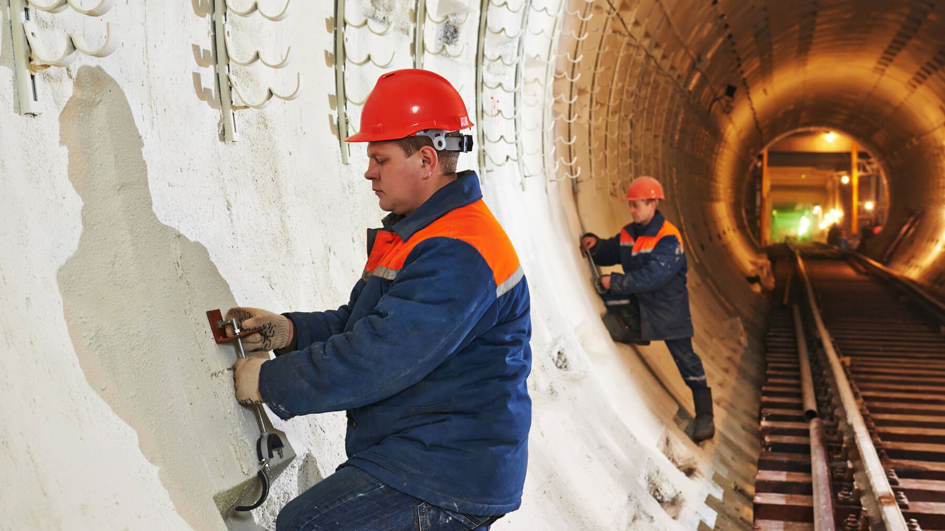Blick in eine Tunnelbaustelle. Eine Person ist im Vordergrund und hantiert mit einem Werkzeug an der Tunnelwand.