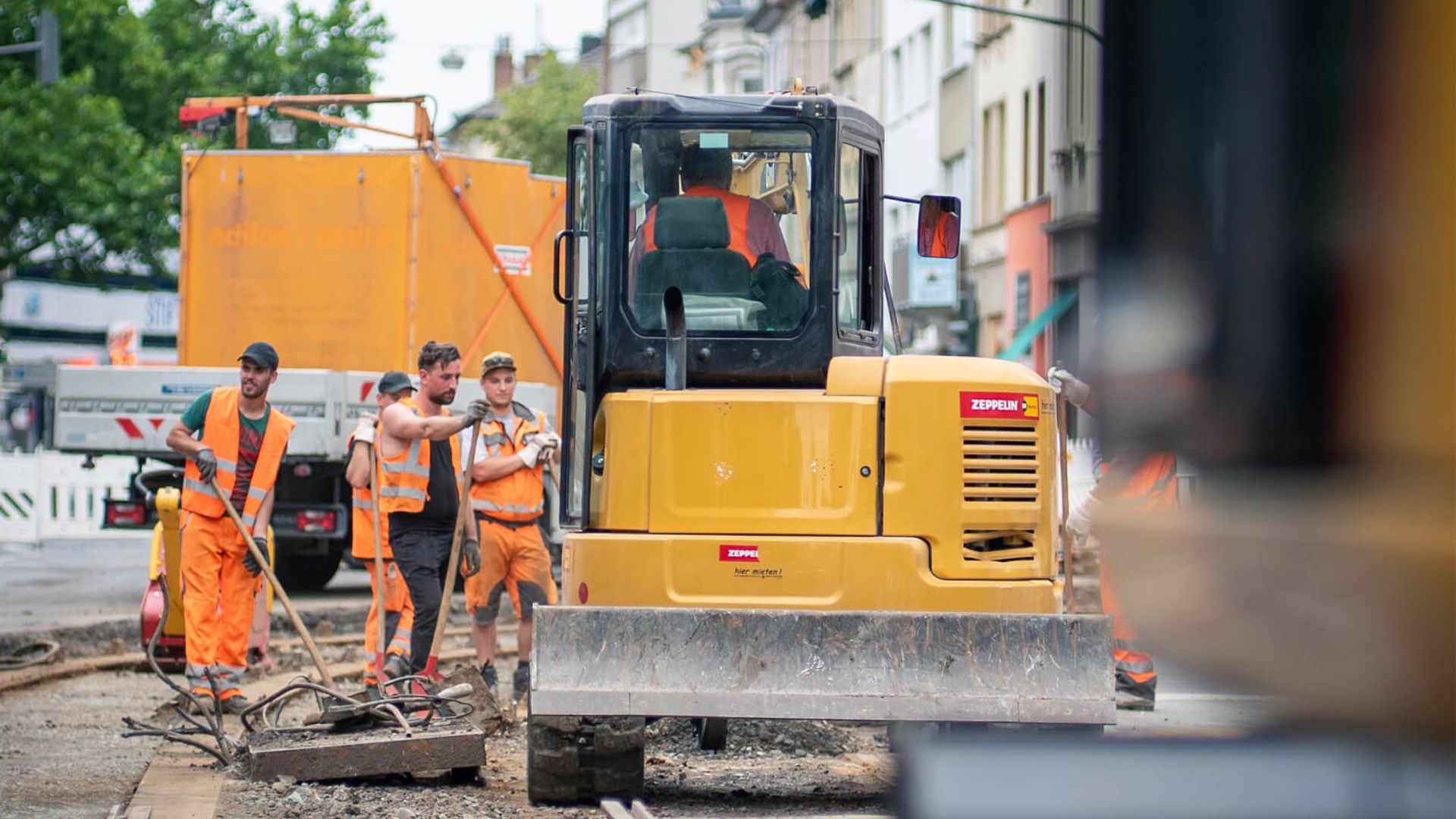 Es sind mehrere Mitarbeiter in Warnwesten und Arbeitskleidung mit Geräten oder Werkzeugen in der Hand zu sehen. 