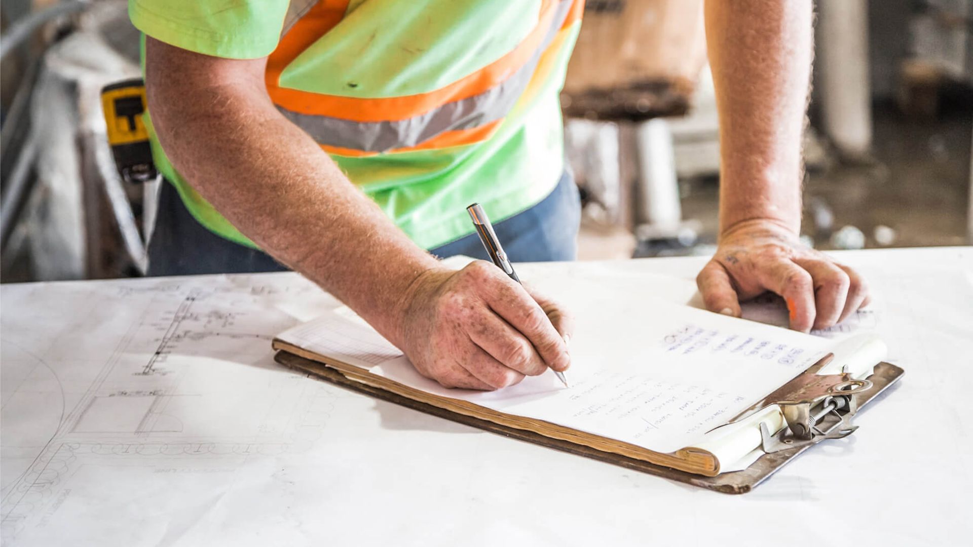Ein Mann mit Warnweste steht vor einem Tisch und schreibt etwas auf eine Liste. 