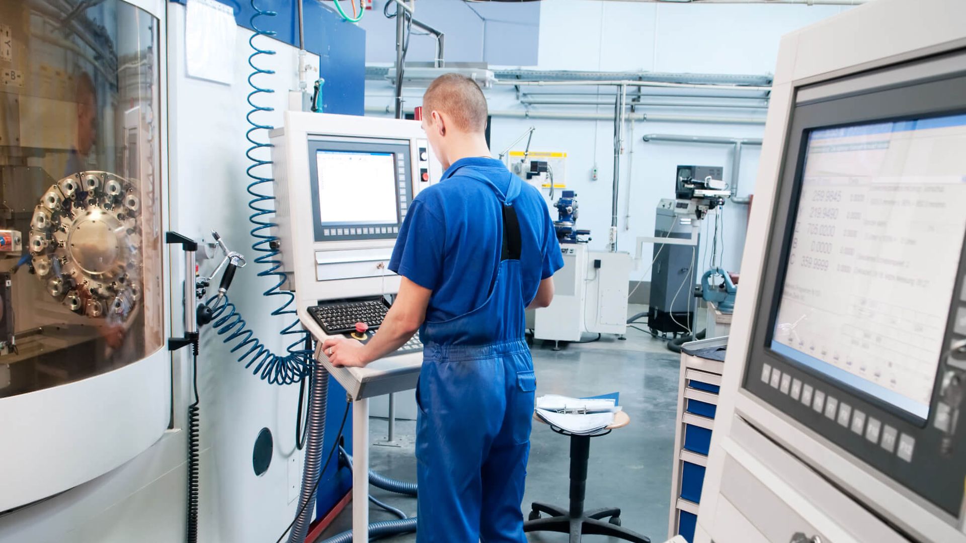 Ein Mann steht vor einem Display einer großen eingehausten Maschine und bedient diese.